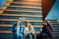 Three young pretty women sit on a bench on a city street, drinking coffee from disposable glasses, talking and laughing Royalty Free Stock Photo