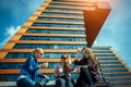 Three young pretty women sit on a bench on a city street, drinking coffee from disposable glasses, talking and laughing. Friends Royalty Free Stock Photo