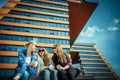 Three young pretty women sit on a bench on a city street, drinking coffee from disposable glasses, talking and laughing. Friends Royalty Free Stock Photo