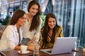 Three young woman sitting in cafe using laptop. One girl showing