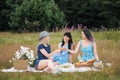 Three young women, blond, brunette and with dyed hair in blue dresses, and hats, sit on plaid and drink wine from Royalty Free Stock Photo