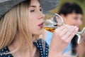 Three young women, blond, brunette and with dyed hair in blue dresses, and hats, sit on plaid and drink wine from Royalty Free Stock Photo