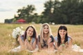 Three young women in blue dresses, and hats lie on plaid and drink wine. Outdoor picnic on grass on beach. Delicious