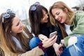 Three young women using a mobile phone in the street. Royalty Free Stock Photo