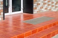 Threshold with a paved red tile and a foot mat at the front door.