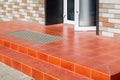 Threshold with a paved red tile and a foot mat at the open front door.