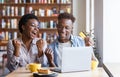 Thrilled black couple with bank card and laptop at cafe