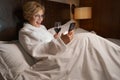 Thrilled woman checking her phone in comfy hotel bed