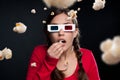 A thrilling experience. Shot of a young woman wearing 3D glasses and eating popcorn against a studio background. Royalty Free Stock Photo