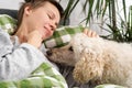 Throughout the day, a woman of middle age, her hair short, rests in bed with her large poodle. Inactivity, weekend ease