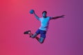 Throwing ball in jump. Young man, professional handball player training, playing isolated over gradient pink background
