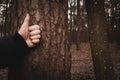 Thumb raised up, hand on tree background in the woodland