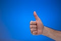 Thumb`s up like gesture made by Caucasian male hand. Close up studio shot, on blue background