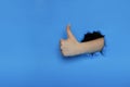 Thumb up hand gesture break through the blue paper wall. female hand showing like Royalty Free Stock Photo