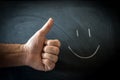 Thumb up beside a smiley face drawn in chalk on a blackboard, concept Royalty Free Stock Photo