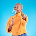 Thumbs up, lollipop and black woman in portrait with candy in studio isolated on a blue background. African person