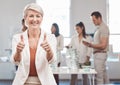 Thumbs up, motivation and yes with a woman leader, manager or CEO working in an office with her team in the background Royalty Free Stock Photo