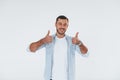Thumbs up. Young handsome man standing indoors against white background Royalty Free Stock Photo
