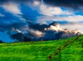 Thunder clouds cresting emerald rolling fields landscape.