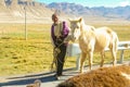 CLOSE UP: Old Tibetan farmer leads beautiful albino horse down an asphalt road.