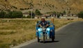 CLOSE UP: Adult Tibetan male rides his old motorbike tricycle down empty road.
