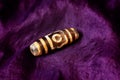 Tibetan amulet dzi bead on a beautiful purple fabric. close-up