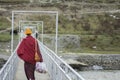 Tibetan monk, with back to the camera, holding groceries in a plastic bag, crossing a bridge