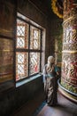 Tibetan old woman praying and turning a big prayer wheel inside a prayer room at Bodnath stupa, in Kathmandu, Nepal. Royalty Free Stock Photo