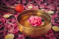 Tibetan singing bowl with floating inside in water pink peony flower. Burning candles, special sticks and petals on the black ston