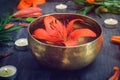 Tibetan singing bowl with floating lily inside. Burning candles, lily flowers and petals on the black wooden background. Meditatio