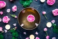 Tibetan singing bowl with floating rose inside. Burning candles, tea rose flowers and petals on the black stone background. Medita