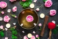 Tibetan singing bowl with floating rose inside. Burning candles, tea rose flowers and petals on the black stone background. Medita