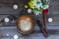 Tibetan singing bowl and special sticks, burning candles and vase with flowers on the dark wooden background, top view. Selective