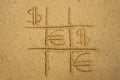 Tic-tac-toe game with playing euro and dollar symbols on sand. Royalty Free Stock Photo