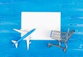 Model of airplane, grocery cart and blank sheet of paper on the blue wooden background. Travel concept. Ticket purchase.