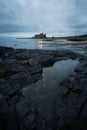 Tidal rockpools lead along the beach towards the ancient Bamburgh Castle where lights can be seen