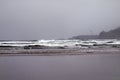 Tide of the Pacific Ocean rolling in along the sandy beach with the lighthouse visible Royalty Free Stock Photo