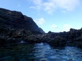 Tide pool on lava rock shore with lighthouse on cliff in distance Royalty Free Stock Photo