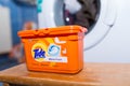 Tide washing liquid capsules in front of a washing machine.