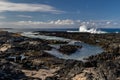 Tidepool on Hawaiian volcanic beach. Black rocks in foreground; sea, blue sky and clouds in background. Royalty Free Stock Photo