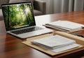 A tidy office desk features a sleek laptop displaying a forest scene Royalty Free Stock Photo