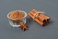 Tied pile of cinnamon sticks near glass bowl full of powder near star of anise lies on dark scratched desk on kitchen Royalty Free Stock Photo