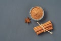 Tied pile of cinnamon sticks near glass bowl full of powder near star of anise lies on dark scratched desk on kitchen Royalty Free Stock Photo