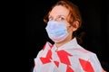 Tied woman with scared eyes in medical mask on a black background, concept. Close-up of redhead girl during coronavirus quarantine