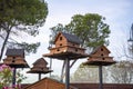 A tiered birdhouse made of wood, painted brown, atop a tall pole with a blue sky in the background