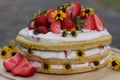 tiered layered cake with yellow wildflowers and strawberries wood board summer cake