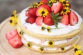 tiered layered cake with yellow wildflowers and strawberries wood board summer cake