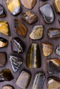 Tiger`s Eye rare jewel on brown wood texture. Sparse mineral pebbles background Royalty Free Stock Photo