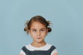 Tight-lipped little girl in striped sweater, hair in buns over blue background. Royalty Free Stock Photo