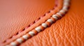 A tight shot of orange leather, displaying a stitching design along its edge The stitching concludes with a distinct white thread Royalty Free Stock Photo